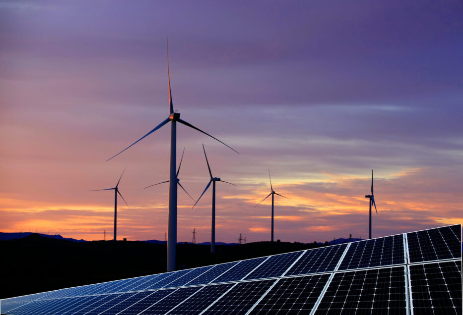 Solar photovoltaic panels and wind turbines in front of a colorful sunset.