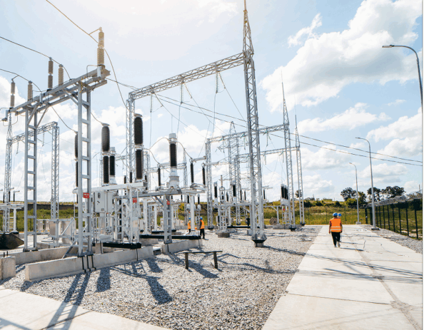 High-voltage transmission substation switchyard with steel structures, electrical equipment, and utility workers on site.