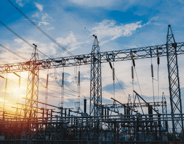 High-voltage transmission substation with steel lattice structures, buswork, and overhead transmission lines at sunset.