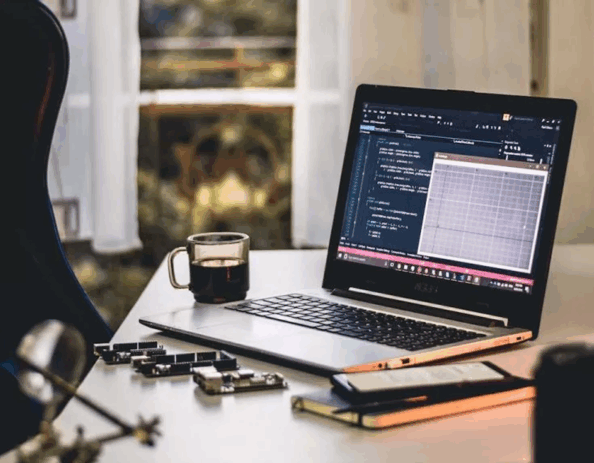 An open laptop with coded data and a cup of coffee on a table.