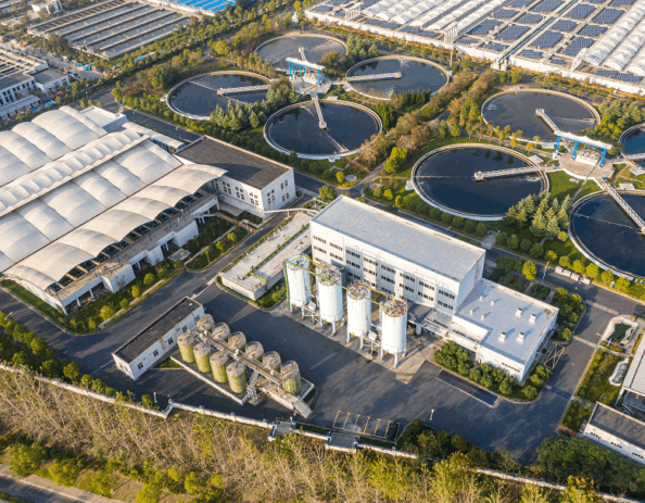 Aerial view of a wastewater treatment plant with circular clarifiers, treatment buildings, and process tanks.