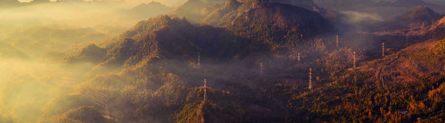 Mountainous region with transmission lines throughout and foggy clouds.